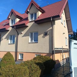 Putz-Mal - Dwupiętrowy dom z beżową elewacją i czerwonym dachem w słoneczny dzień. Widoczne rusztowania i częściowo samochód dostawczy. Ujęcie z dołu.