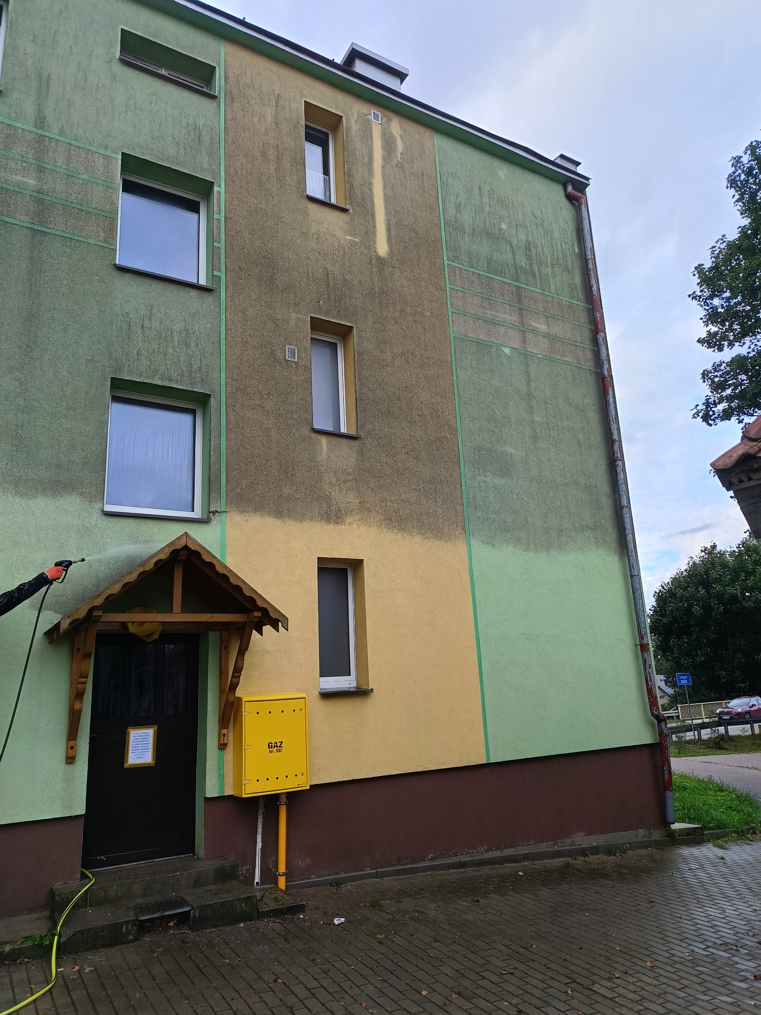 Czyszczenie elewacji budynku wielorodzinnego z widocznym efektem różnicy czystości. Część elewacji jest już umyta, a część jeszcze zabrudzona.