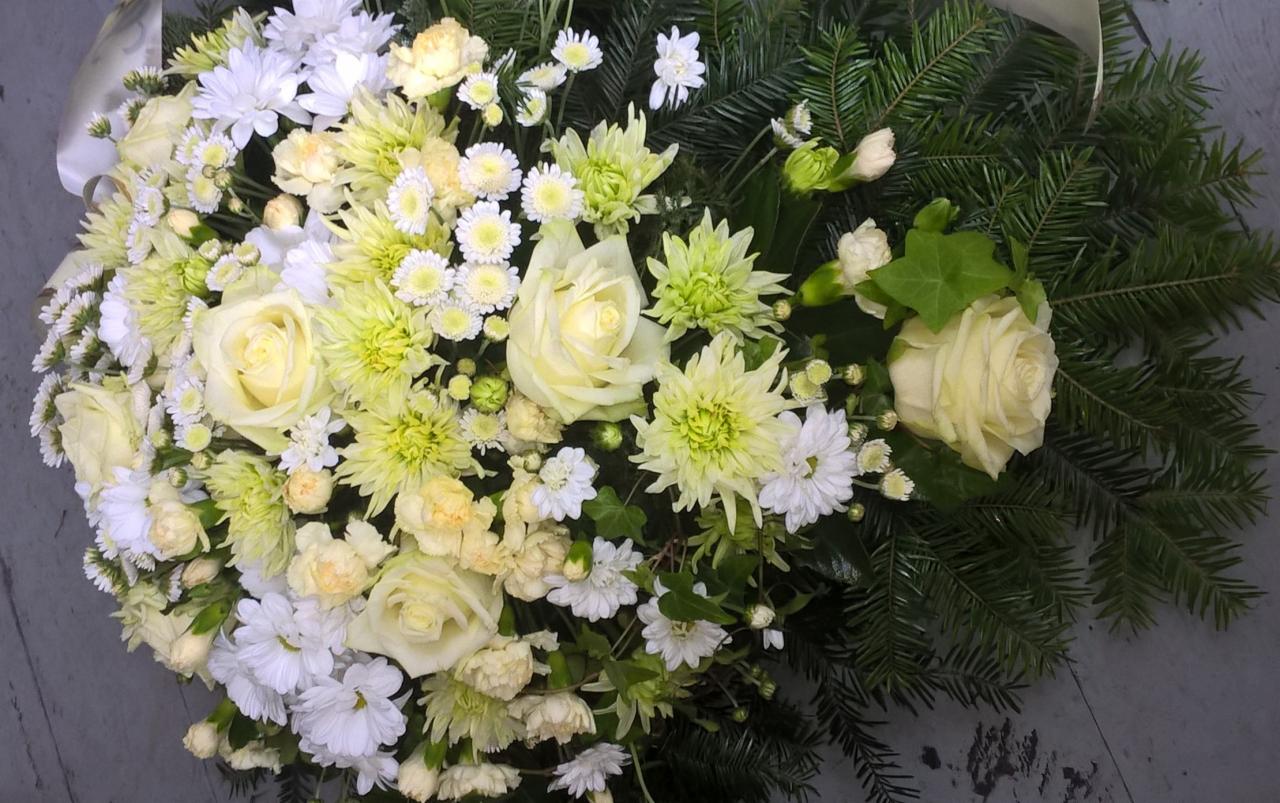 Kompozycja kwiatowa z białych i kremowych róż, chryzantem i drobnych białych kwiatów, uzupełniona zielonymi gałązkami świerku i wstążką.