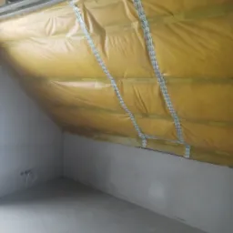 Montaż folii paroizolacyjnej na skośnym poddaszu, widoczne metalowe profile i taśma uszczelniająca, surowy stan wykończenia wnętrza.