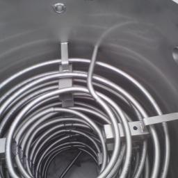 FRENO Spółka z ograniczoną odpowiedzialnością - Wnętrze zbiornika z rurą spiralną ze stali nierdzewnej, wspawaną w kilku punktach do ścianek zbiornika, widoczne otwory montażowe.