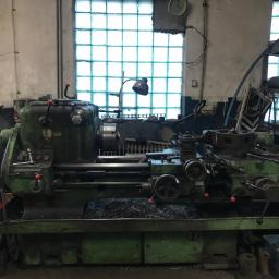 FRENO Spółka z ograniczoną odpowiedzialnością - Stare, zielone urządzenie tokarskie z widocznymi wiórami metalowymi na prowadnicach, ustawione w warsztacie z oknem z luksferami w tle.