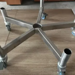 Stalowa podstawa z pięcioma ramionami zakończonymi rurami i kółkami, leżąca na drewnianym blacie, z widocznymi spawami.