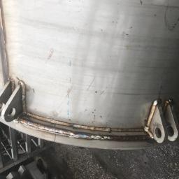 FRENO Spółka z ograniczoną odpowiedzialnością - Fragment spawanej, metalowej konstrukcji cylindrycznej z uchwytami, widoczne ślady po spawaniu i niebieskie oznaczenia.