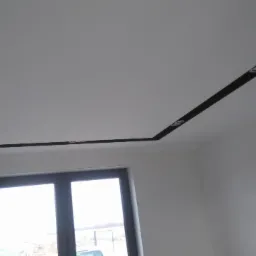 Biały sufit podwieszany z czarnymi wstawkami i wbudowanymi punktowymi lampami LED, widok z dołu, okno w tle.