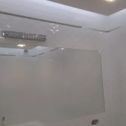 Biała łazienka z płytkami o wzorze rombów, lustrem w srebrnej ramie i ozdobną lampą kryształową nad lustrem.