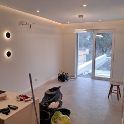 Usługi Remontowe - Jasne wnętrze po remoncie z nowoczesnym oświetleniem, sprzętem budowlanym i widokiem na ogród przez przesuwne drzwi balkonowe.