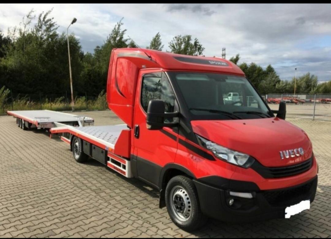 Czerwona laweta Iveco z platformą na przyczepie, zaparkowana na kostce brukowej w Lublinie, z widocznym logo Spokmar na dachu kabiny.