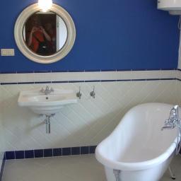 King-Dom - Biała łazienka z niebieskimi akcentami, owalne lustro z odbiciem osoby robiącej zdjęcie, bateria wannowa wolnostojąca, biała umywalka na ścianie, biało-niebieskie płytki ułożone w karo.