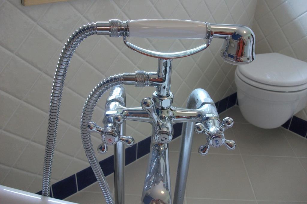 Bateria wannowa chromowana z wężem prysznicowym i słuchawką, z porcelanową rączką, na tle płytek w romby z granatowym akcentem i wiszącej toalety.