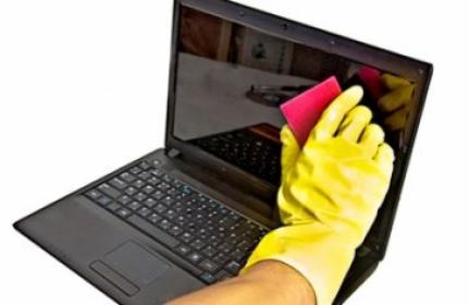 Czyszczenie ekranu laptopa ściereczką przez osobę w żółtej rękawiczce ochronnej.