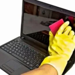 Czyszczenie ekranu laptopa ściereczką w rękawicy ochronnej, widoczne odbicie klawiatury w wyłączonym ekranie.