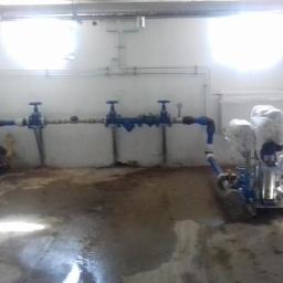 Hydro-Team - Piwnica z zainstalowanym systemem rur i zaworów, widoczne również pompy owinięte folią ochronną, na podłodze ślady wilgoci.