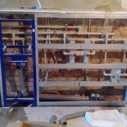 Hydro-Team - Stelaż podtynkowy z widoczną instalacją hydrauliczną, rury z tworzywa sztucznego, ściana z cegły w tle, faza montażu.