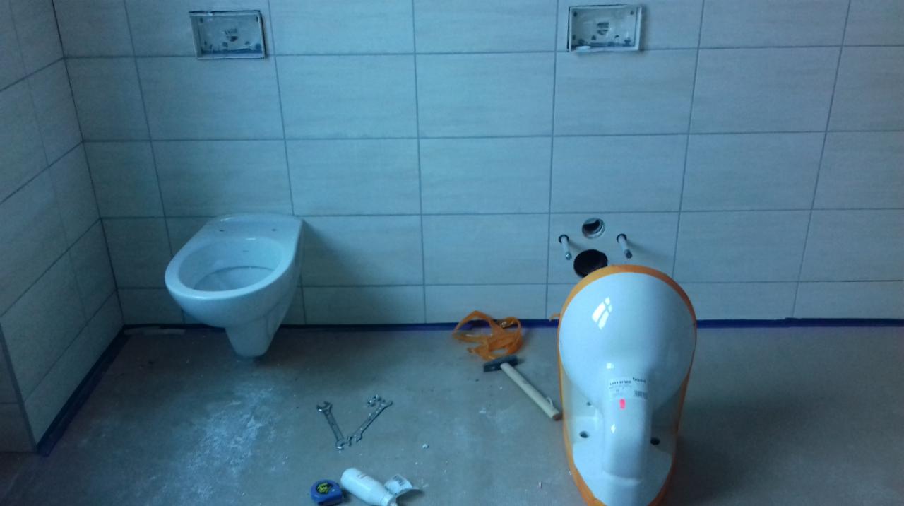 Wnętrze łazienki w trakcie montażu podwieszanej toalety, widoczne płytki ceramiczne na ścianach, instalacja podtynkowa, narzędzia i akcesoria instalacyjne na podłodze.