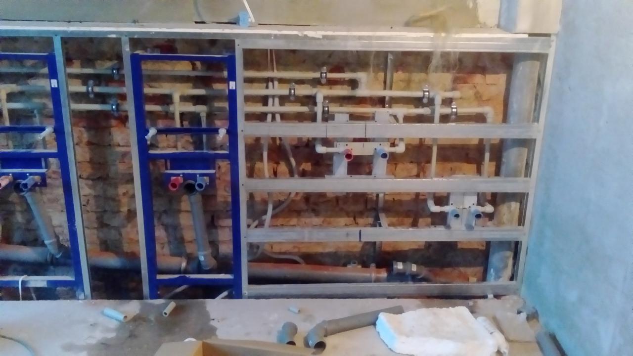 Stelaż podtynkowy z widoczną instalacją hydrauliczną, rury z tworzywa sztucznego, ściana z cegły w tle, faza montażu.