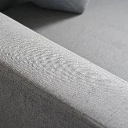 Szczegółowe ujęcie szarej, teksturowanej tapicerki kanapy z wyraźnym szwem i subtelnym cieniowaniem.