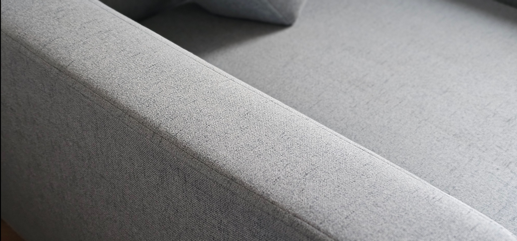 Szczegółowe ujęcie szarej, teksturowanej tapicerki kanapy z wyraźnym szwem i subtelnym cieniowaniem.