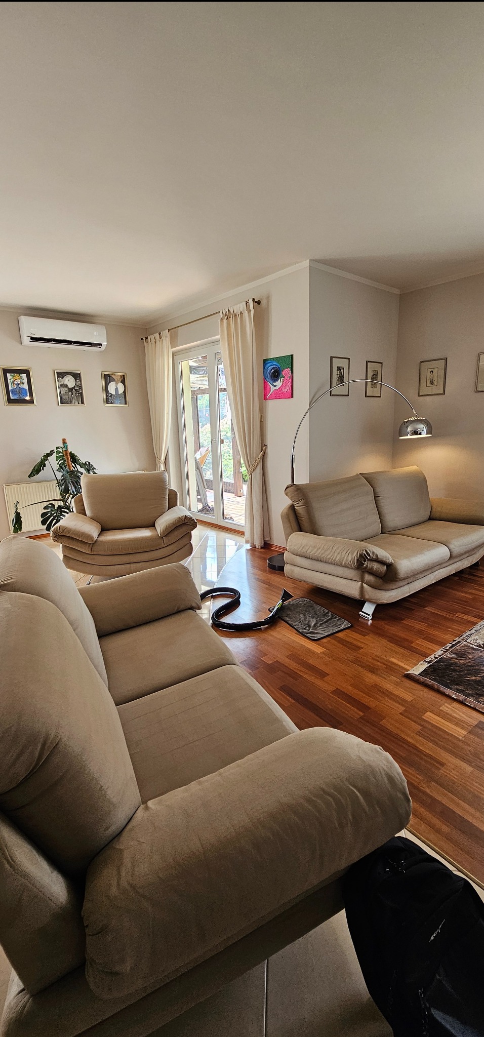 Salon z beżowymi meblami tapicerowanymi i sprzętem do czyszczenia tapicerki na drewnianej podłodze, widok na taras