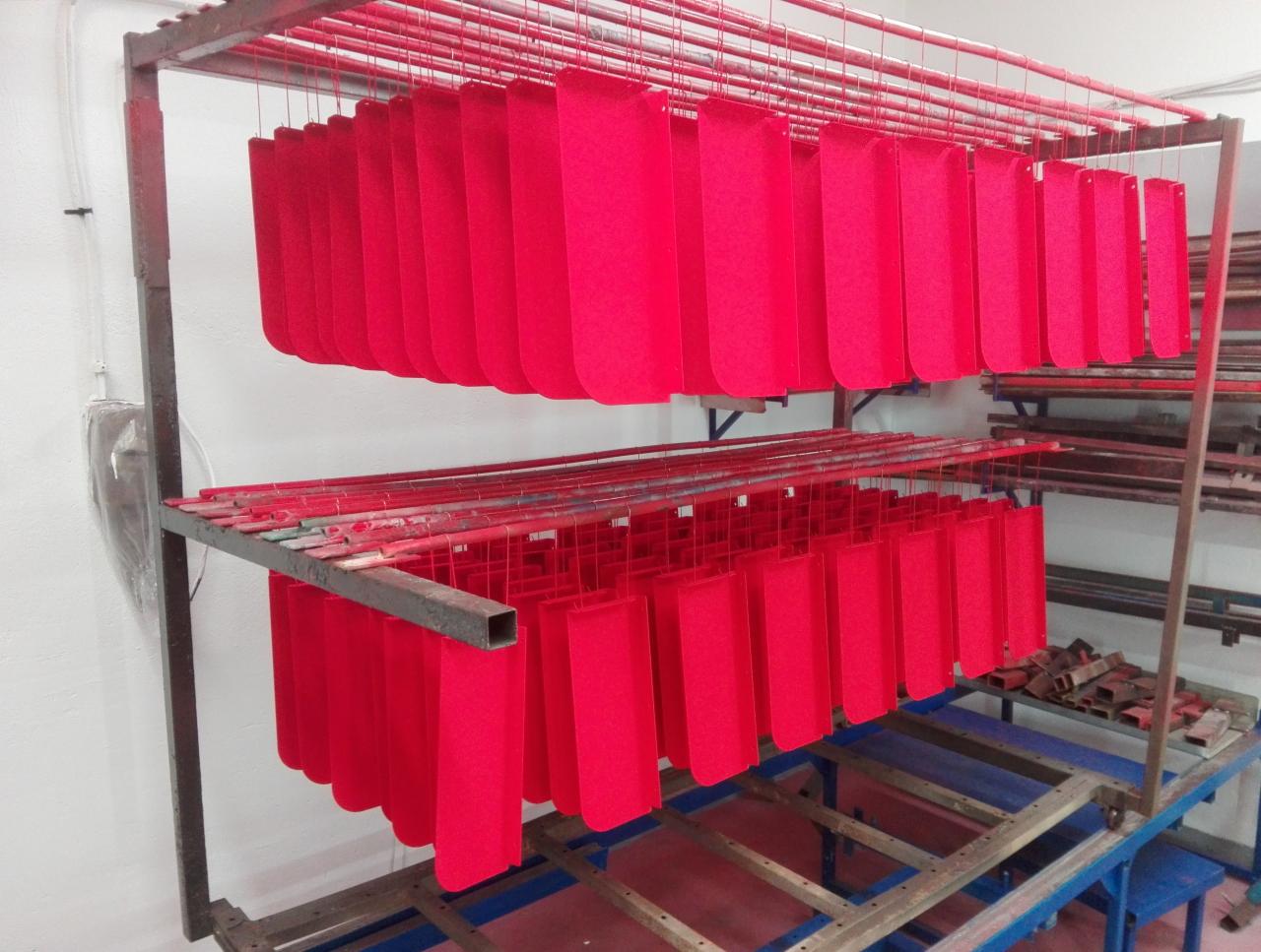 Czerwone, pomalowane proszkowo elementy zawieszone na metalowym regale w hali produkcyjnej, gotowe do dalszej obróbki lub transportu.