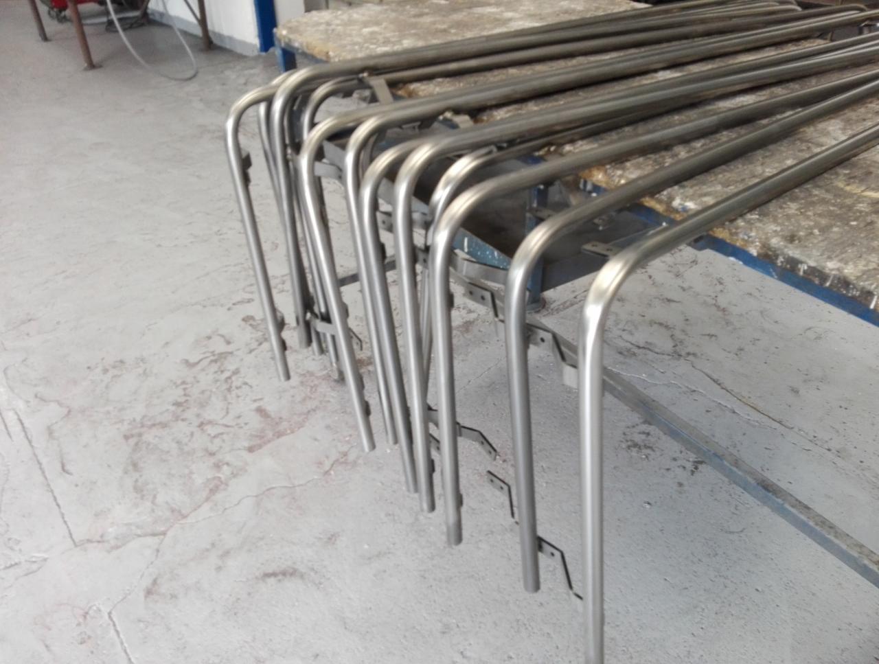 Szereg giętych, metalowych rur ułożonych na stole warsztatowym, widoczne ślady obróbki.