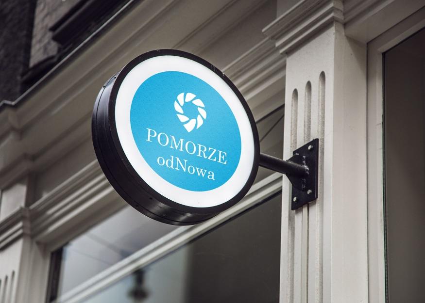 Elegancki, okrągły szyld reklamowy z podświetleniem, w kolorach błękitu i bieli, przymocowany do fasady budynku z oknami, prezentujący logo i nazwę 'POMORZE odNowa'.