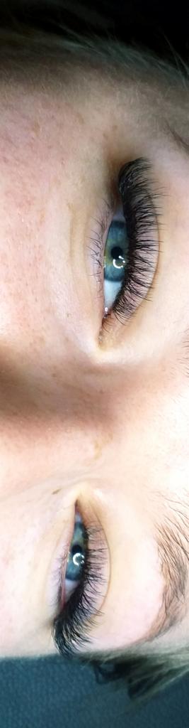 Zbliżenie na oko z przedłużonymi, gęstymi rzęsami w stylu Hollywood, widoczne drobne piegi na skórze powiek.