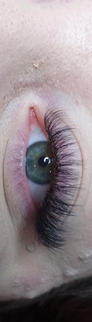 Zbliżenie na oko z przedłużonymi, gęstymi rzęsami; widoczna tęczówka w odcieniach zieleni i niebieskiego, oraz drobne niedoskonałości skóry wokół oka.