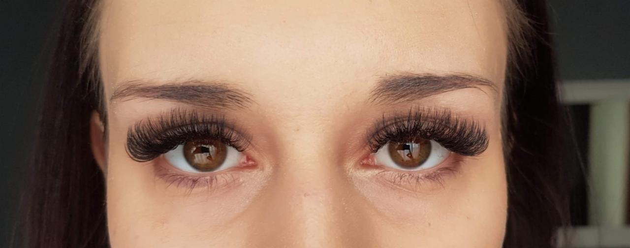 Zbliżenie na oczy kobiety z brązowymi tęczówkami i gęstymi, przedłużonymi rzęsami w stylu 'kocie oko', podkreślone delikatnym makijażem brwi.