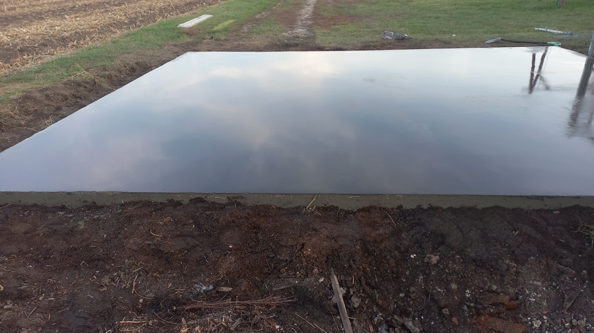 Świeżo wylana, gładka betonowa wylewka na przygotowanym podłożu ziemnym, odbijająca niebo jak lustro.