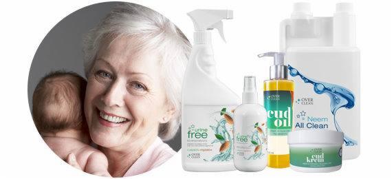 Uśmiechnięta kobieta trzymająca niemowlę obok zestawu środków czystości ekologicznych w białych opakowaniach z zielonymi akcentami i napisami.