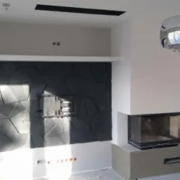 Nowoczesny salon z kominkiem i ścianą dekoracyjną z paneli 3D, podświetlony wiszącą lampą kryształową.