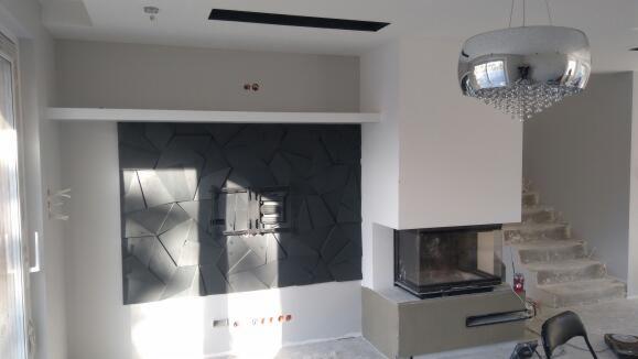 Nowoczesny salon z kominkiem i ścianą dekoracyjną z paneli 3D, podświetlony wiszącą lampą kryształową.