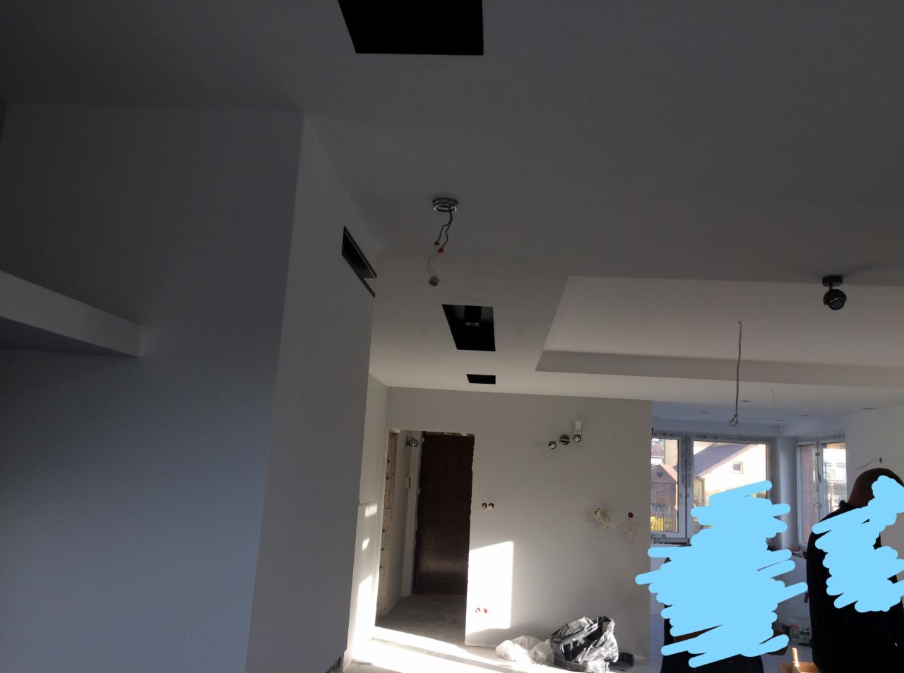 Wnętrze po malowaniu na biało, widoczne przygotowania do montażu oświetlenia w suficie podwieszanym, z pozostawionymi kablami i otworami montażowymi.