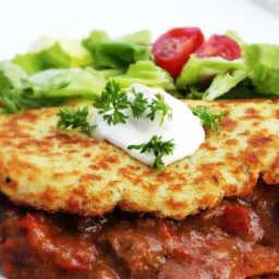 Placki ziemniaczane na gulaszu z kleksem śmietany i natką pietruszki, podane z sałatką ze świeżych warzyw.