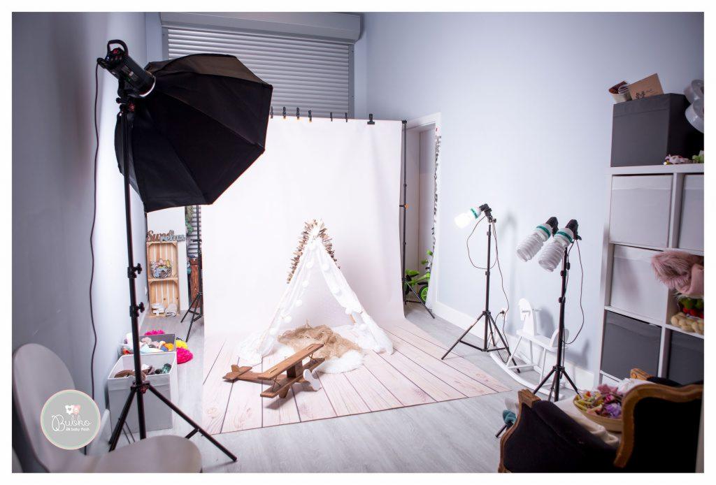 Studio fotograficzne z białym tłem, namiotem tipi ozdobionym lampkami, drewnianym samolotem, lampami studyjnymi i rekwizytami do sesji noworodkowej lub dziecięcej