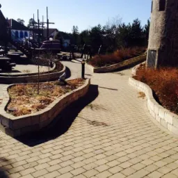 Ścieżka z kostki brukowej w parku rozrywki z motywem zamku i statku pirackiego w tle, otoczona murkami z kostki.