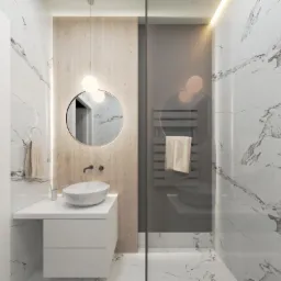Nowoczesna łazienka z marmurowymi płytkami, okrągłym lustrem podświetlanym od tyłu i wiszącą umywalką na białej szafce, z widoczną kabiną prysznicową ze szklaną ścianą i grzejnikiem drabinkowym.