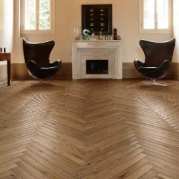 Parkiet ułożony we wzór jodełki francuskiej w przestronnym salonie z kominkiem i dwoma fotelami typu Egg, oświetlony naturalnym światłem z okien.