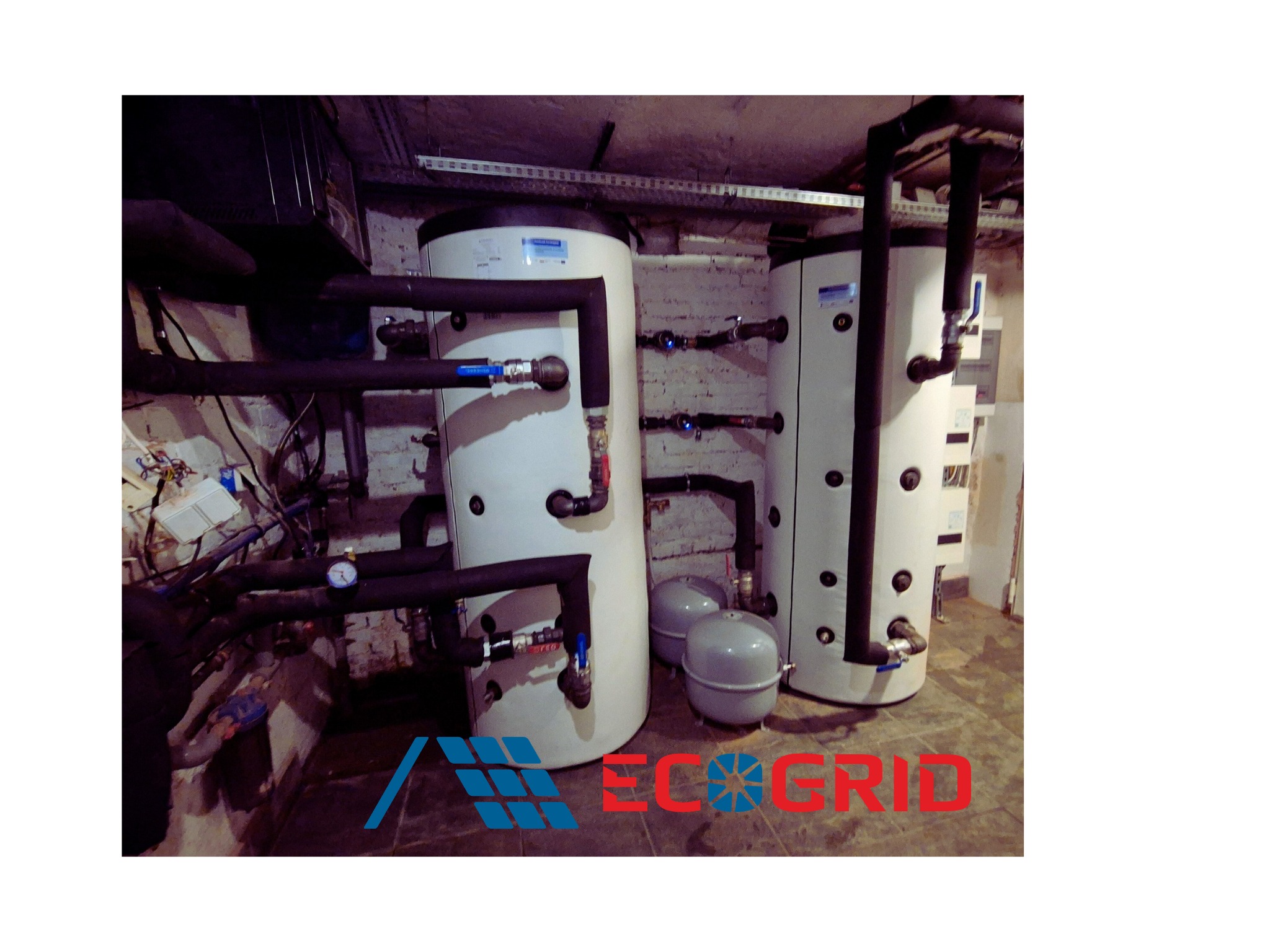 Kotłownia z dwoma buforami CO 2x500L i kaskadą pomp ciepła Panasonic Aquarea 64kW. Rury, zawory, manometr. Widoczne logo firmy na pierwszym planie.