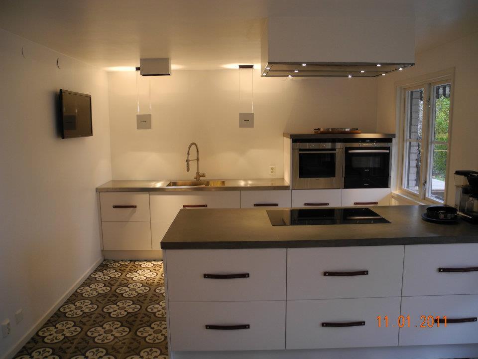 Nowoczesna kuchnia z białymi szafkami z brązowymi uchwytami, szarym blatem, wzorzystą podłogą i sprzętem AGD ze stali nierdzewnej.