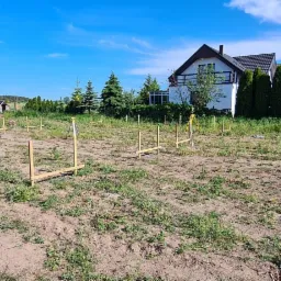 Wytyczanie fundamentów domu jednorodzinnego na działce, widoczne drewniane szalunki i niwelator optyczny.