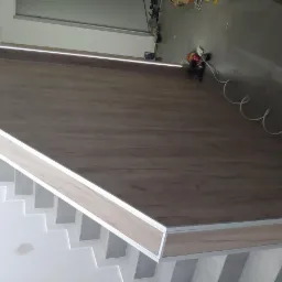 Ściana i schody wykończone panelami imitującymi drewno z ukrytym oświetleniem LED, widoczne narzędzia i kable na podłodze w tle.