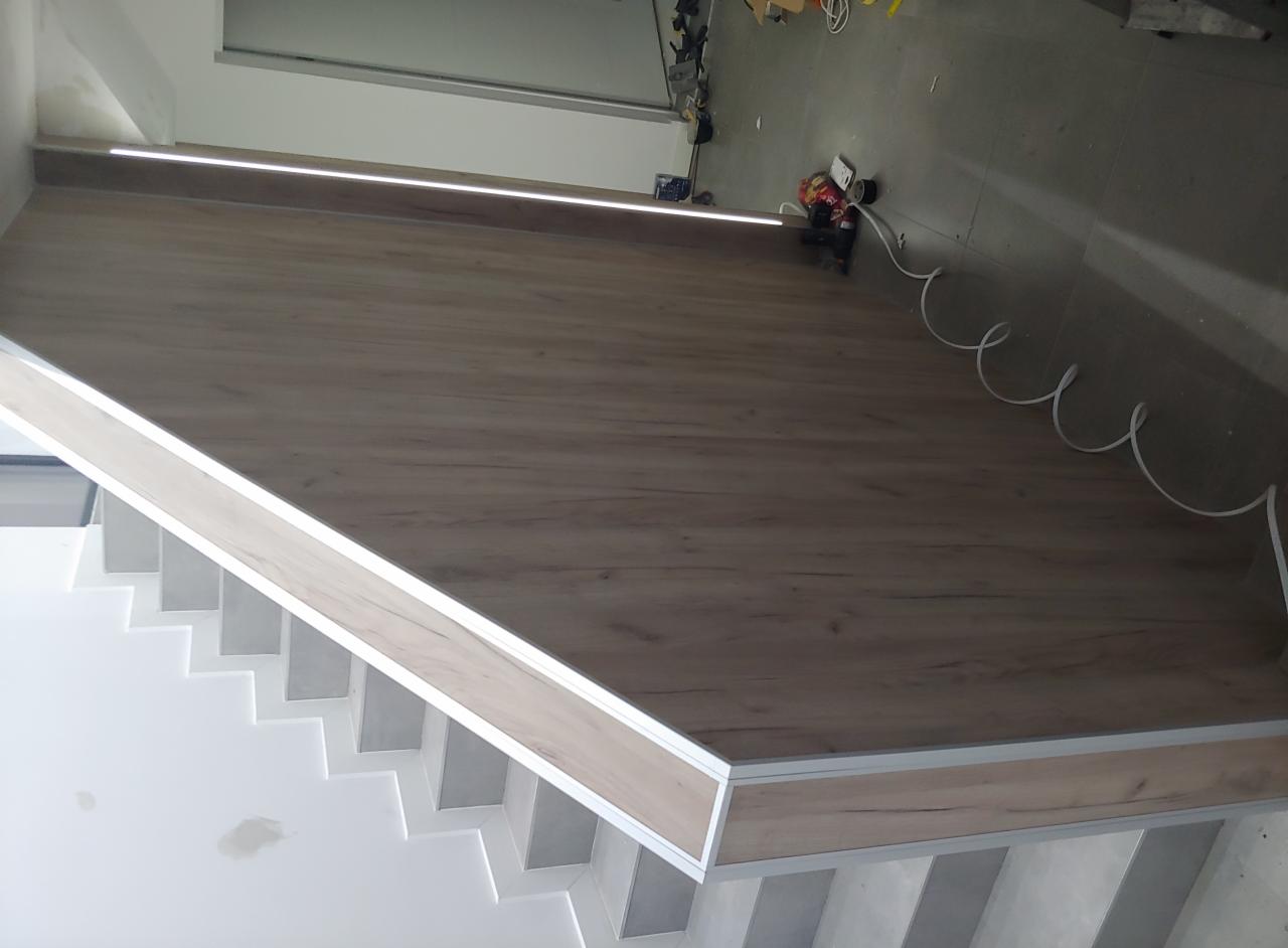 Ściana i schody wykończone panelami imitującymi drewno z ukrytym oświetleniem LED, widoczne narzędzia i kable na podłodze w tle.