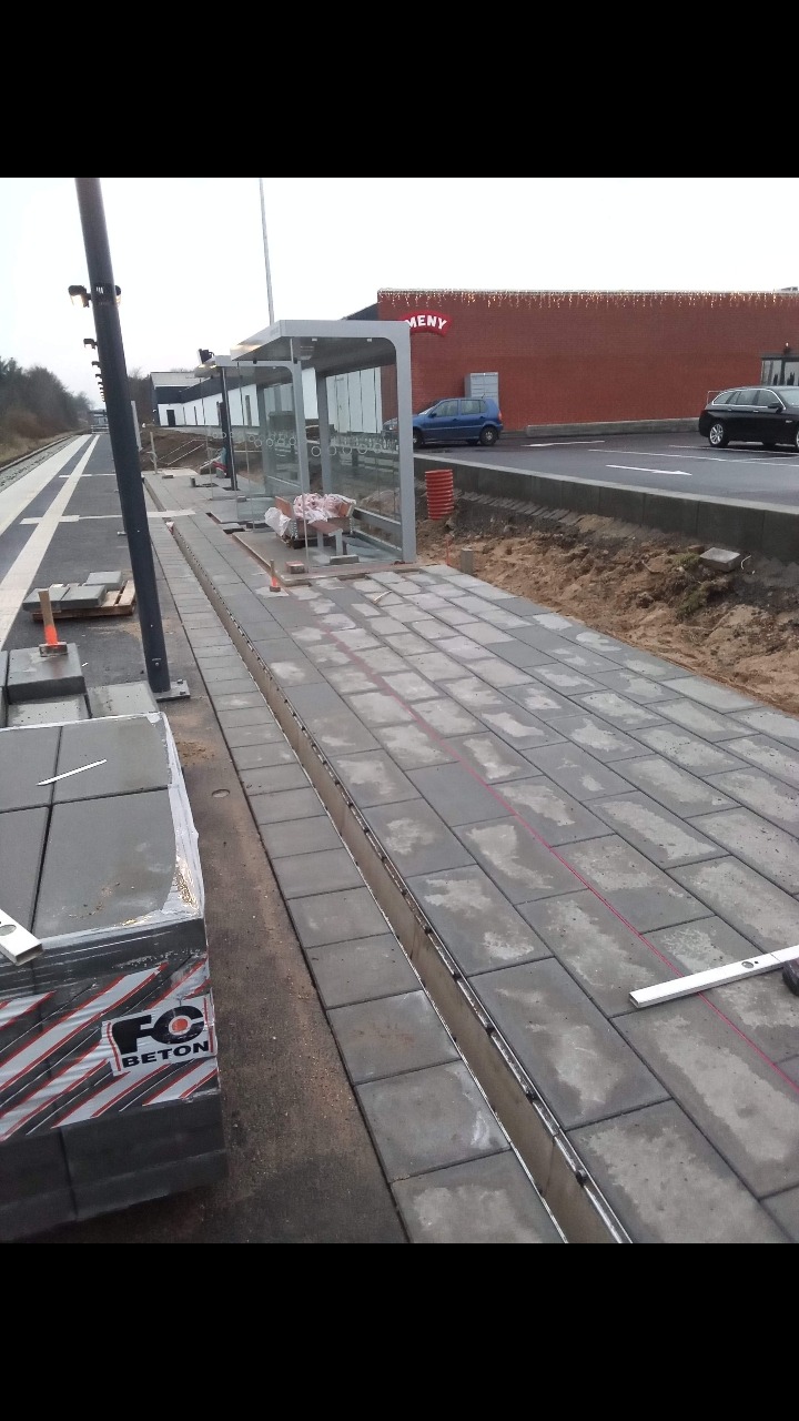 Etap układania szarej kostki brukowej prostokątnej na peronie, widoczne paczki kostki, poziomica i wytyczone linie.