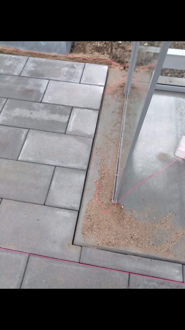 Etap prac brukarskich w Żninie: widoczne szare prostokątne kostki ułożone częściowo, wyznaczające krawędź tarasu lub ścieżki, z użyciem sznurka traserskiego i metalowego profilu.