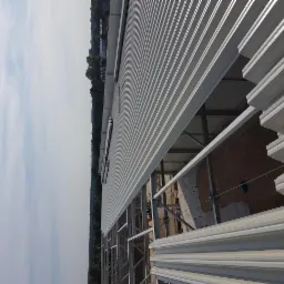 Montaż blachy trapezowej na konstrukcji stalowej budynku przemysłowego, widoczne niekompletne fragmenty poszycia i ślady po starym murze.