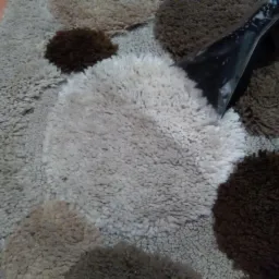 Dysza odkurzacza piorącego na tle wzorzystego dywanu z okrągłymi elementami o różnej kolorystyce i fakturze.