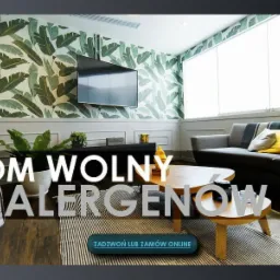 Nowoczesny salon z tapetą w liście, szarą sofą z żółtymi poduszkami i drewnianym stolikiem kawowym, z hasłem 'Dom wolny od alergenów' na pierwszym planie.