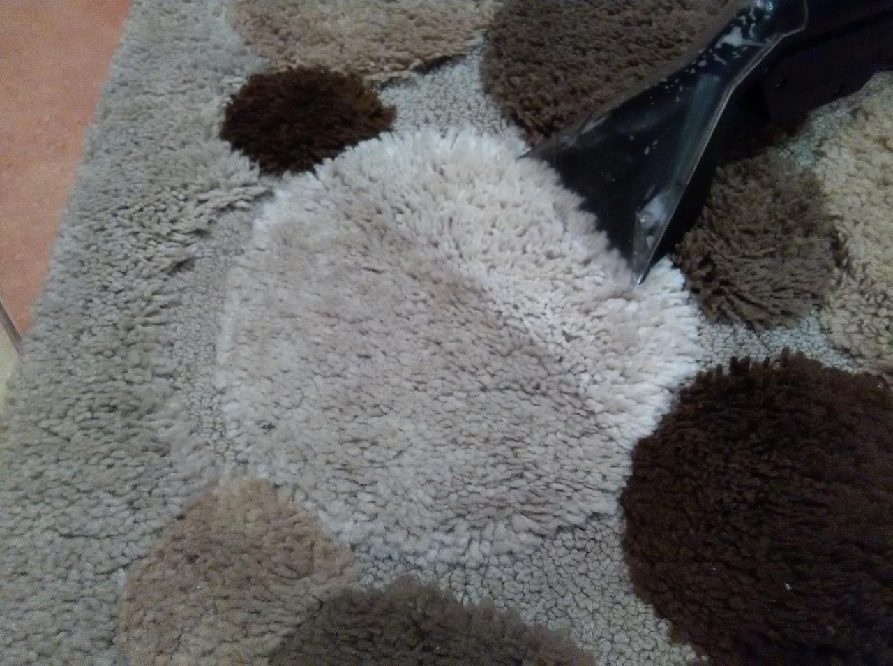 Dysza odkurzacza piorącego na tle wzorzystego dywanu z okrągłymi elementami o różnej kolorystyce i fakturze.